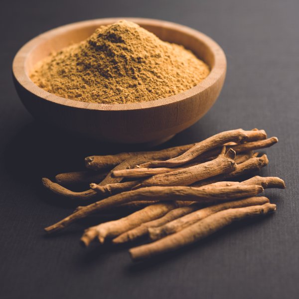 Ašvagandos milteliai dubenėlyje ir šone ašvagandos šaknys padėtos